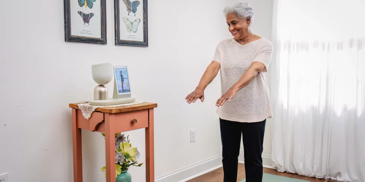 ElliQ being used by an older woman who is working out on a green yoga mat.