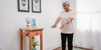 ElliQ being used by an older woman who is working out on a green yoga mat.