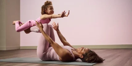 A smiling mother and her young daughter doing yoga together on mats in a bright living room
