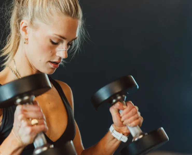 A woman wearing a Second Wind Nasal strip while lifting weights.