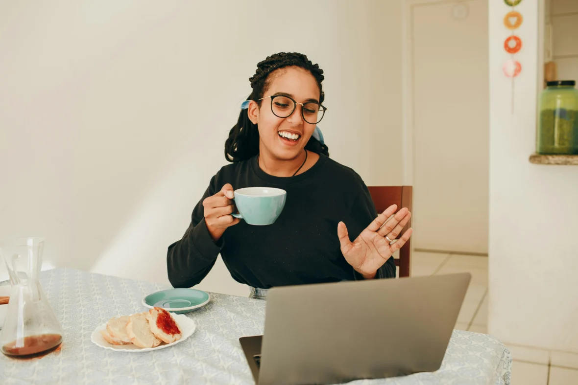 a woman on a telehealth call on her laptop and drinking coffee.