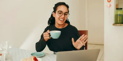 a woman on a telehealth call on her laptop and drinking coffee.
