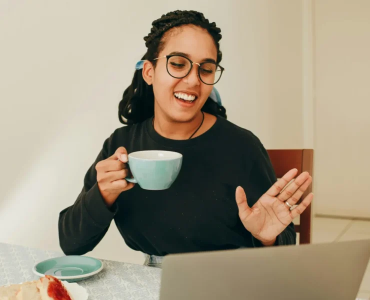 a woman on a telehealth call on her laptop and drinking coffee.