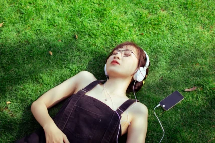 A woman listening to music on her headphones in a grassy field.