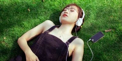 A woman listening to music on her headphones in a grassy field.