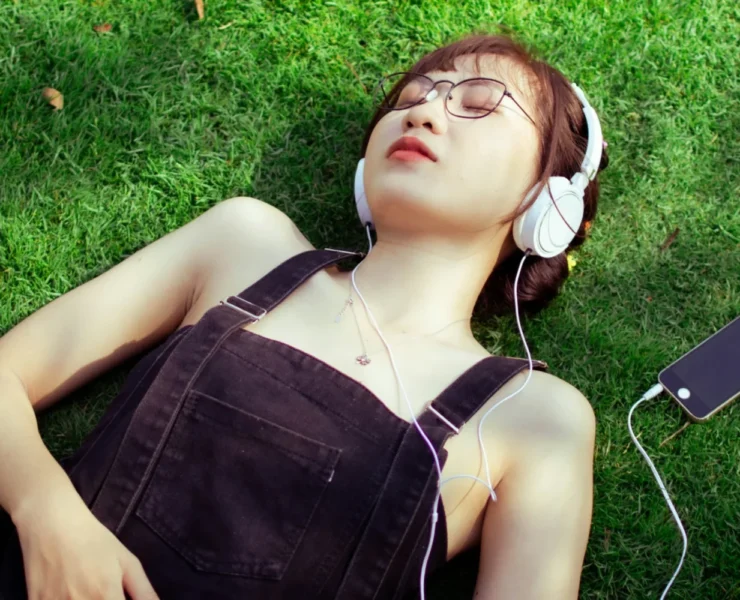 A woman listening to music on her headphones in a grassy field.