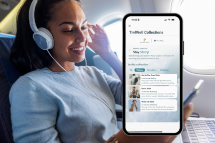 A woman on a plan looking at her phone and wearing headphones.