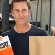 Tom Brady outdoors holding a pack of GOAT Gummies and a GOPUFF bag.