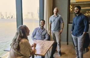 a group of people talk together in a room overlooking the ocean