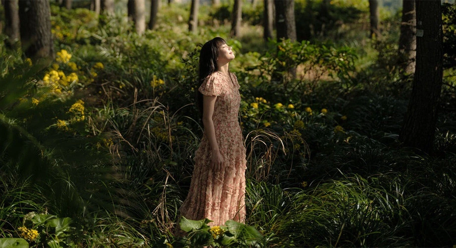 A woman wandering in the woods and looking up at the sky.