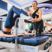 A woman trainer at JetSet Pilates assisting a client on a Reformer.