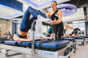 A woman trainer at JetSet Pilates assisting a client on a Reformer.