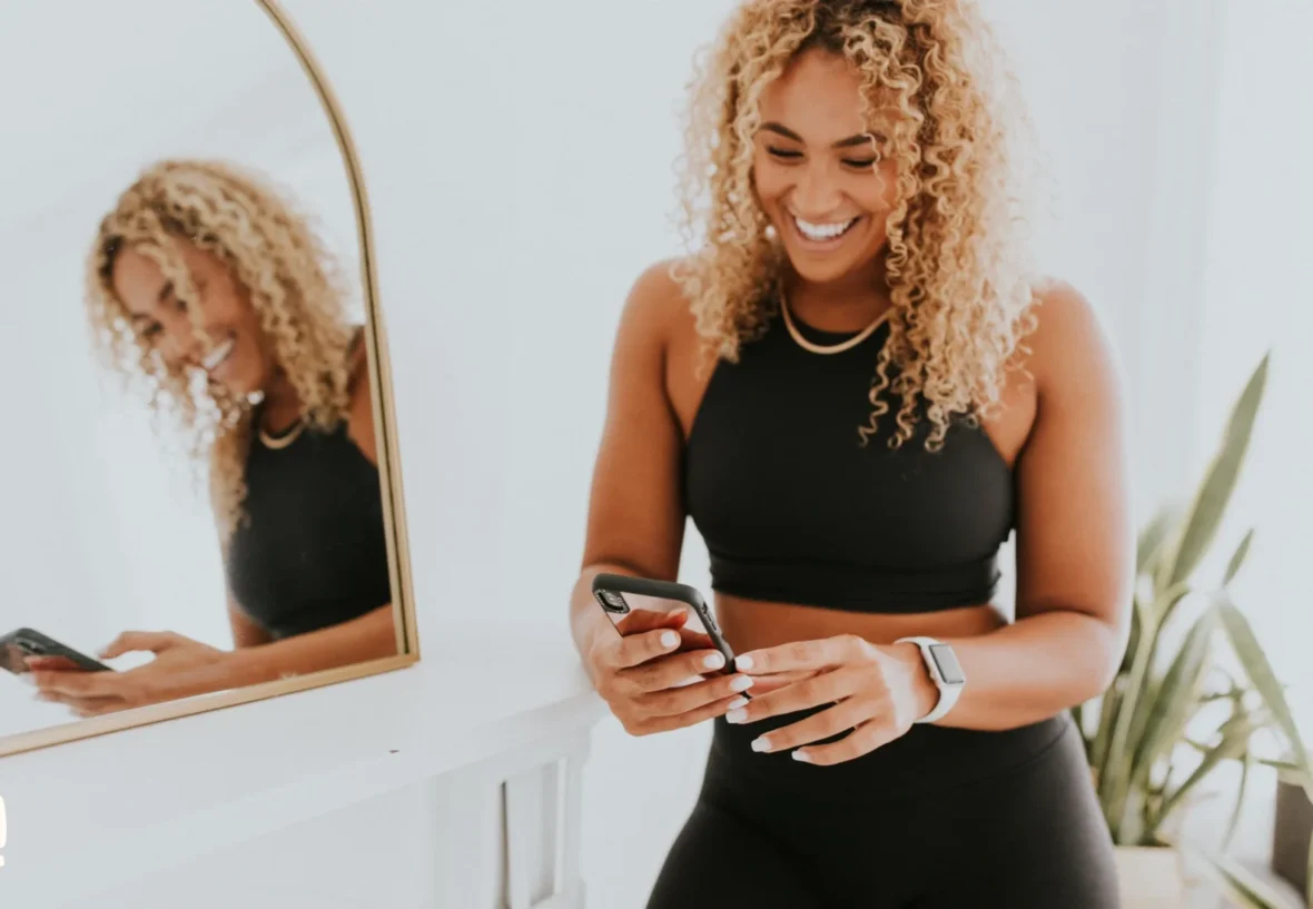 A woman looking at her phone in front of a mirror.