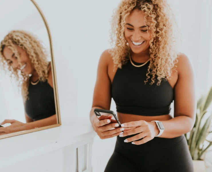 A woman looking at her phone in front of a mirror.