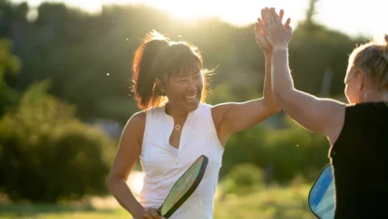 two people high-fiving with a pickleball paddle in a woman's hand