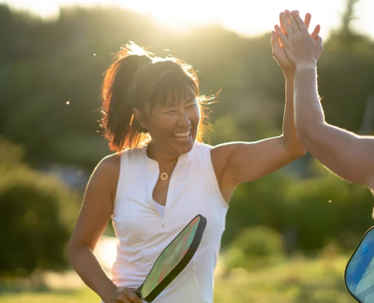 two people high-fiving with a pickleball paddle in a woman's hand