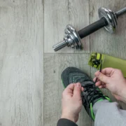 A man lacing up his sneaker with a water bottle and weight in the background.