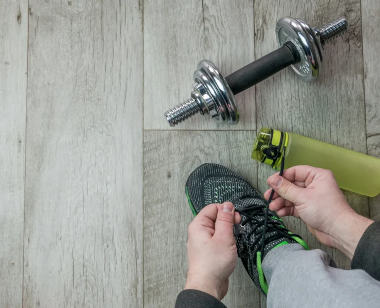 A man lacing up his sneaker with a water bottle and weight in the background.