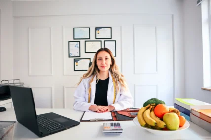 A woman sitting at desk by a fruit bowl and a computer.
