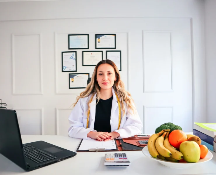 A woman sitting at desk by a fruit bowl and a computer.
