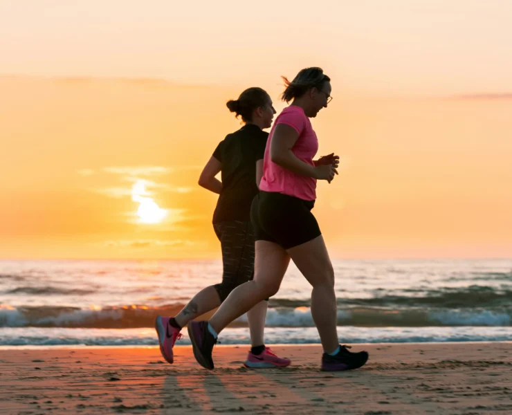 two women running on the beach during the sunset