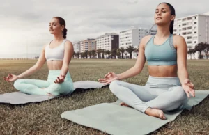 two young women do yoga outside
