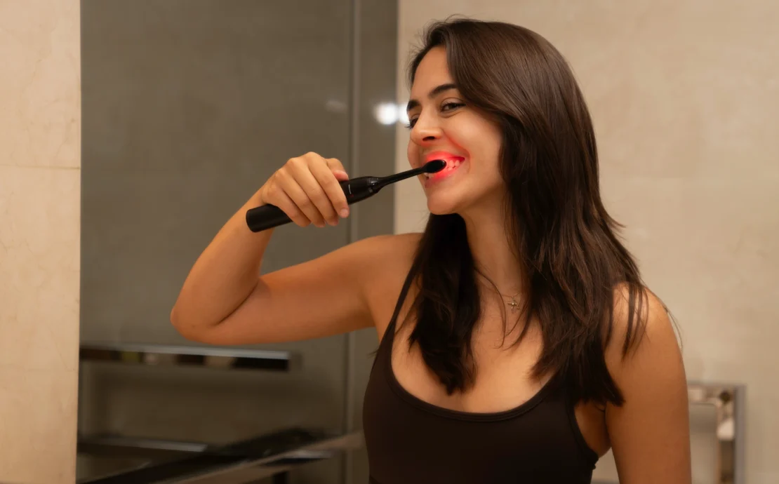 woman brushing her teeth with red light toothbrush