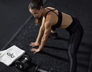 woman works out next to an Alo towel and Alo dumbbells