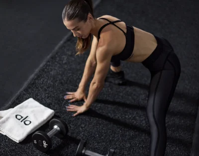 woman works out next to an Alo towel and Alo dumbbells