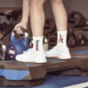 woman picks up a kettlebell wearing reebok sneakers