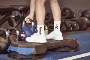 woman picks up a kettlebell wearing reebok sneakers