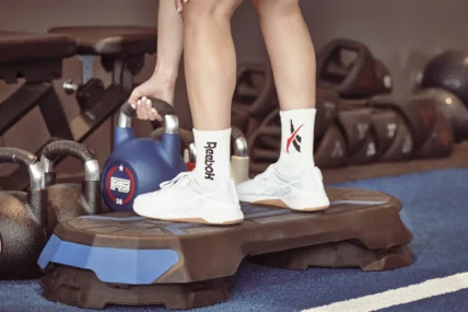 woman picks up a kettlebell wearing reebok sneakers