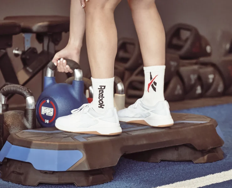 woman picks up a kettlebell wearing reebok sneakers