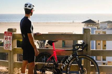 man stands next to a bike while overlooking the beach