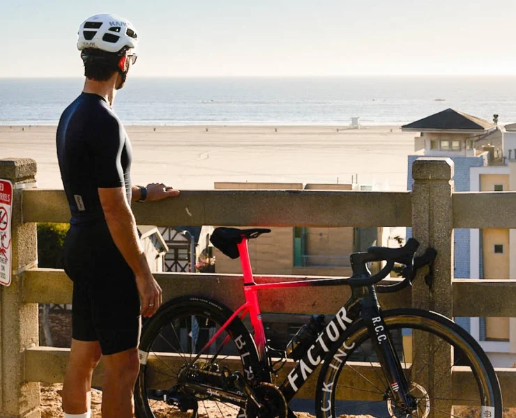 man stands next to a bike while overlooking the beach