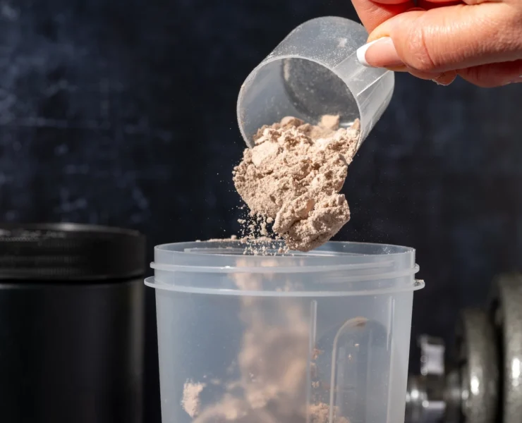 woman pours protein powder into a shaker bottle
