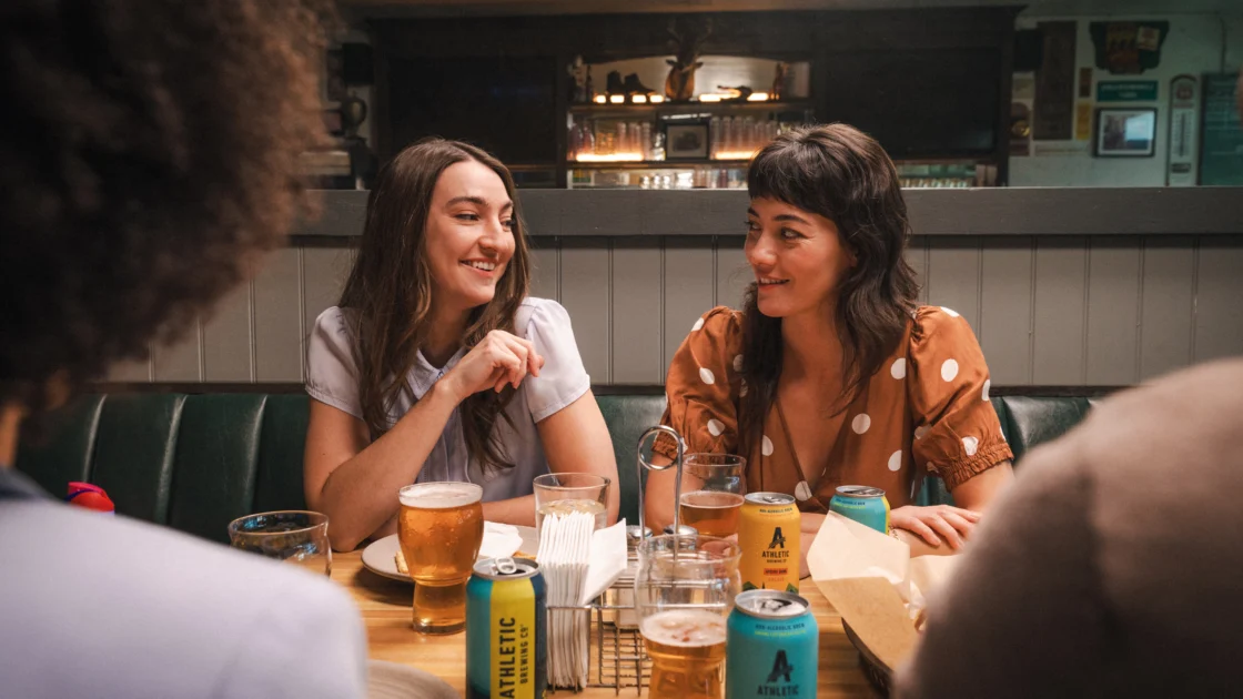 Friends socializing at a bar while drinking Athletic Brewing non-alcoholic beer, highlighting alcohol-free craft beer in a casual dining setting