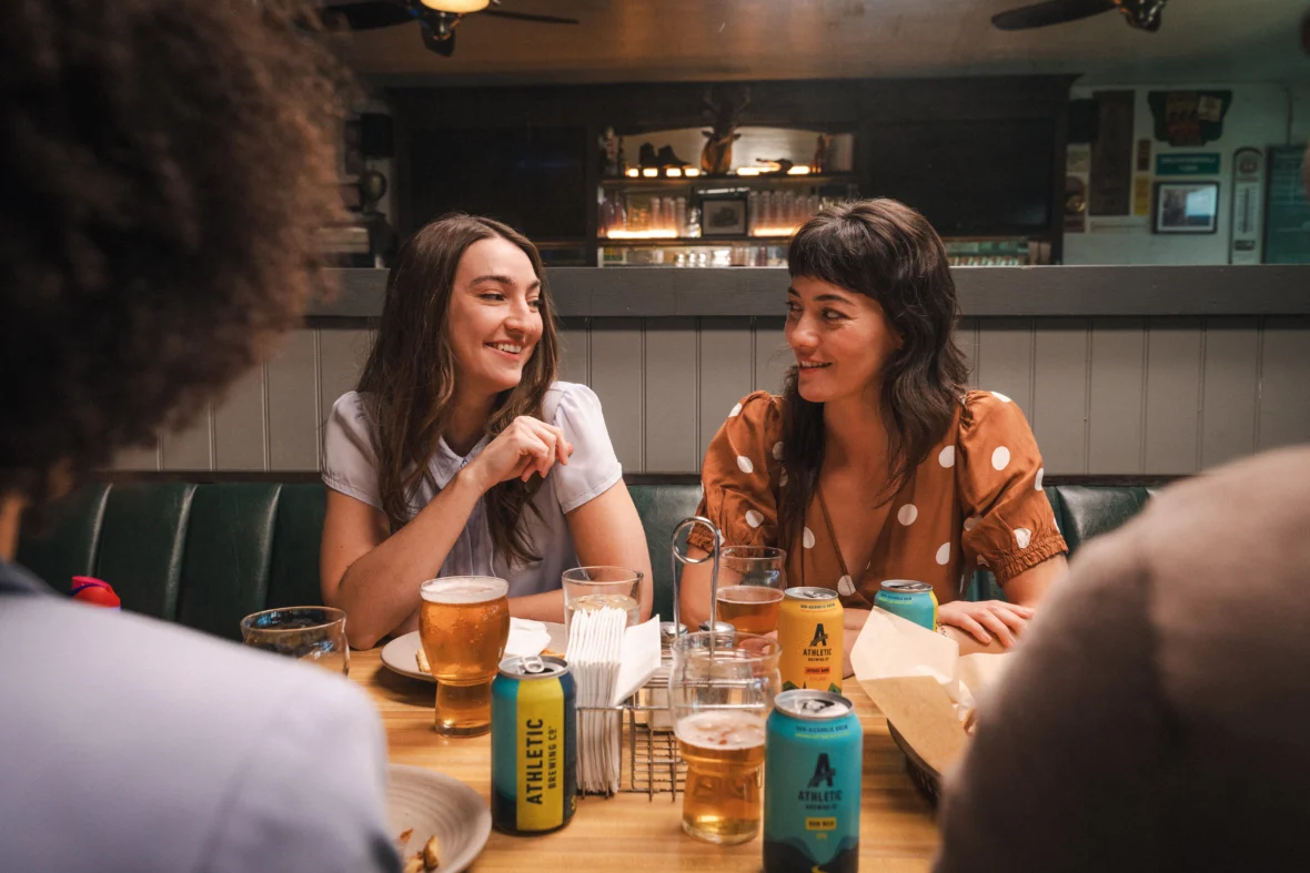 Friends socializing at a bar while drinking Athletic Brewing non-alcoholic beer, highlighting alcohol-free craft beer in a casual dining setting