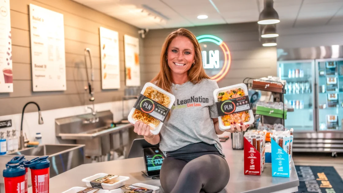 A woman holding Project LeanNation meals in a kitchen.