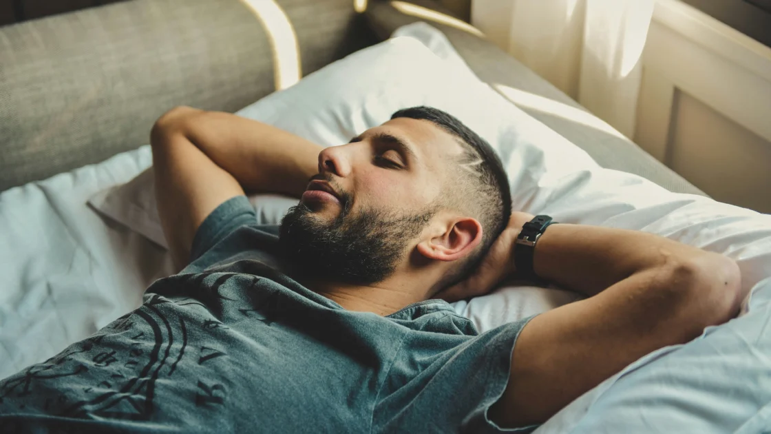 A man sleeping in bed with a watch on his wrist.