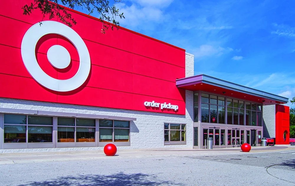 Exterior of a Target store with a bright red facade, large bullseye logo and an order pickup entrance under a blue sky.