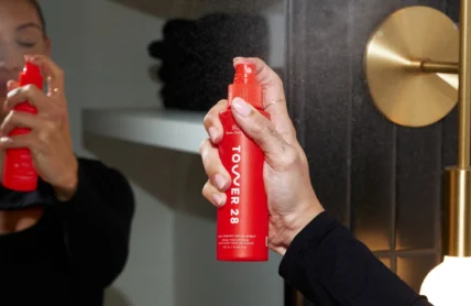 woman sprays a Tower 28 bottle