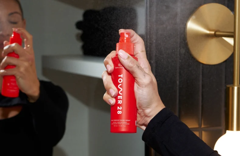 woman sprays a Tower 28 bottle