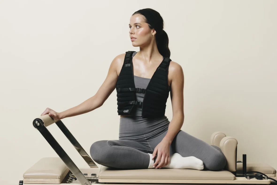 A woman on a Pilates reformer wearing a Stakt vest.