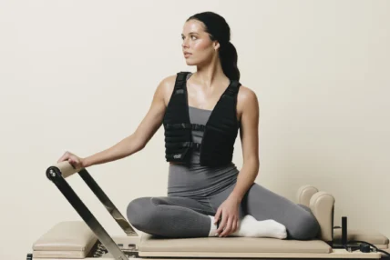 A woman on a Pilates reformer wearing a Stakt vest.