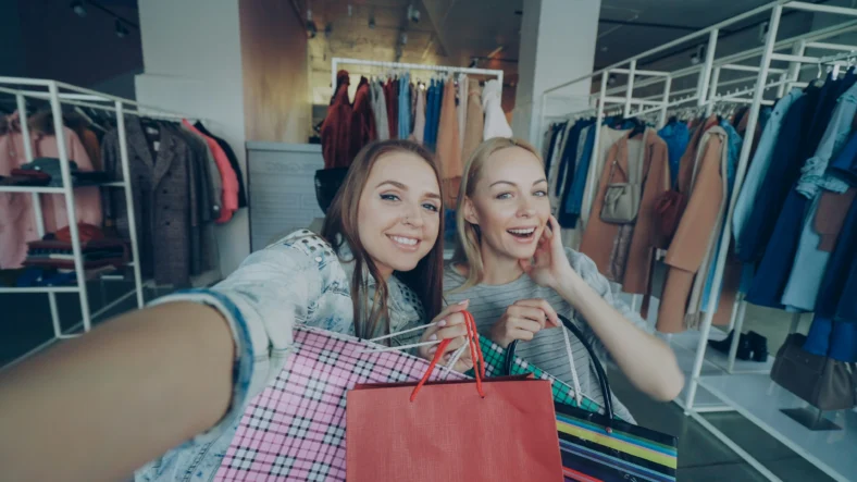 Two young women holding shopping bags while live-stream shopping.