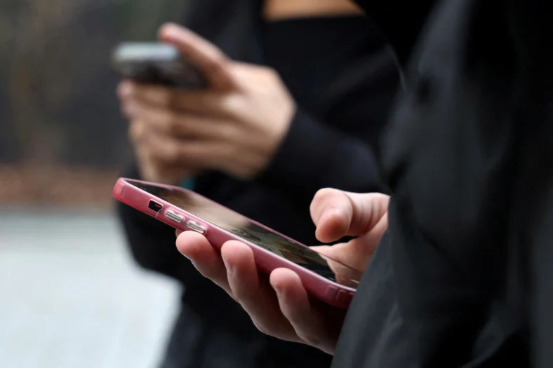 Teenagers look at their mobile phone screens in Paris, France, February 20, 2026.