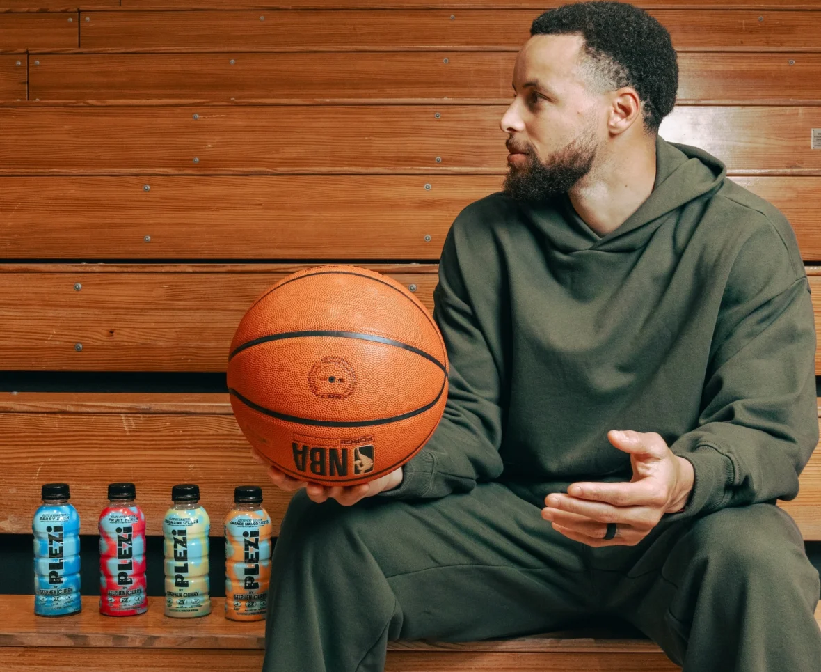 Steph Curry holds a basketball next to Plezi bottles