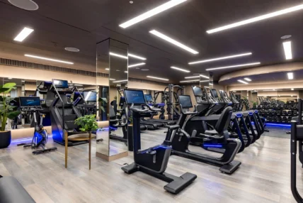 Modern luxury hotel gym with ONYX cardio machines, treadmills, bikes and dumbbell rack, mirrored walls, wood flooring and LED lighting.